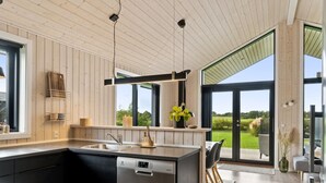 Una cocina moderna con lavavajillas, armarios de madera y un amplio ventanal con vistas a un jardín.