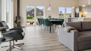 Een moderne woonkamer met een bank, een eettafel met stoelen, een open haard en een keukenhoek met een raam.