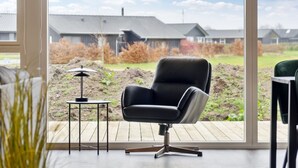 Een moderne kamer met een groot raam, een zwarte lederen fauteuil en een klein tafeltje met een lamp.