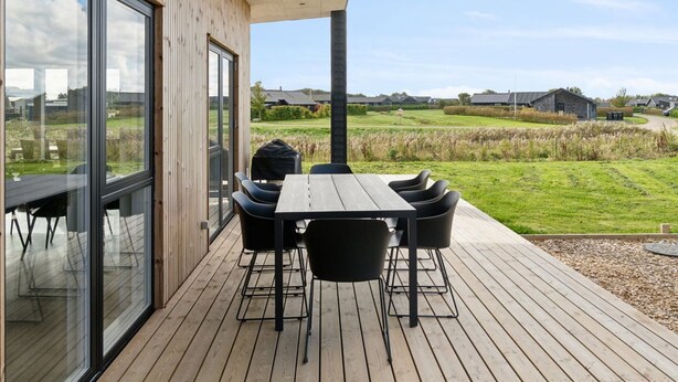 Een houten terras met een tafel en stoelen, met uitzicht op een grasveld en gebouwen in de verte.