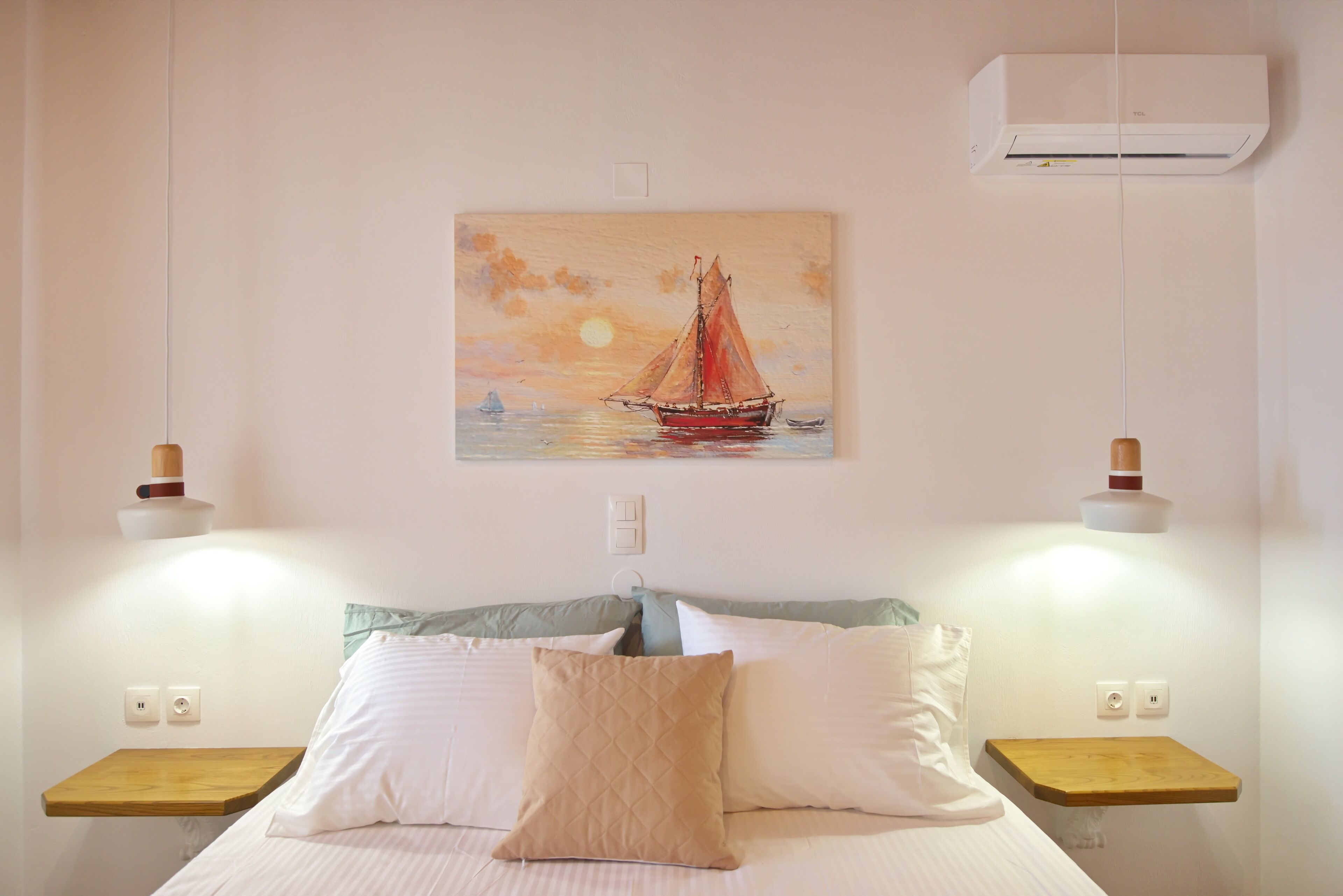 Ein Schlafzimmer mit Bett, Kissen, Nachttischen, einer Wand-Klimaanlage und einem Gemälde eines Segelboots.