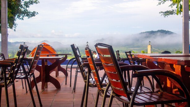 A terrace with tables and chairs, overlooking a mountainous landscape with fog. - Sabay Farm (Kampot)