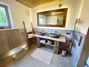 A bathroom with a wooden vanity, two stone sinks, a large mirror, and a towel rack. - Chalet Alpflower (Halblech)