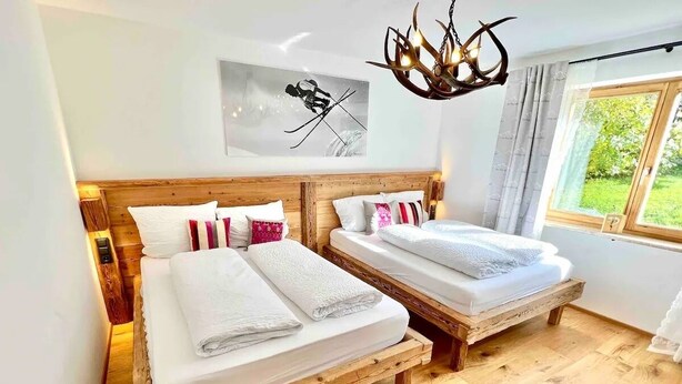 Un dormitorio con dos camas de madera, ropa de cama blanca, un cabecero de madera, una araña, una ventana con cortinas y un cuadro en la pared.