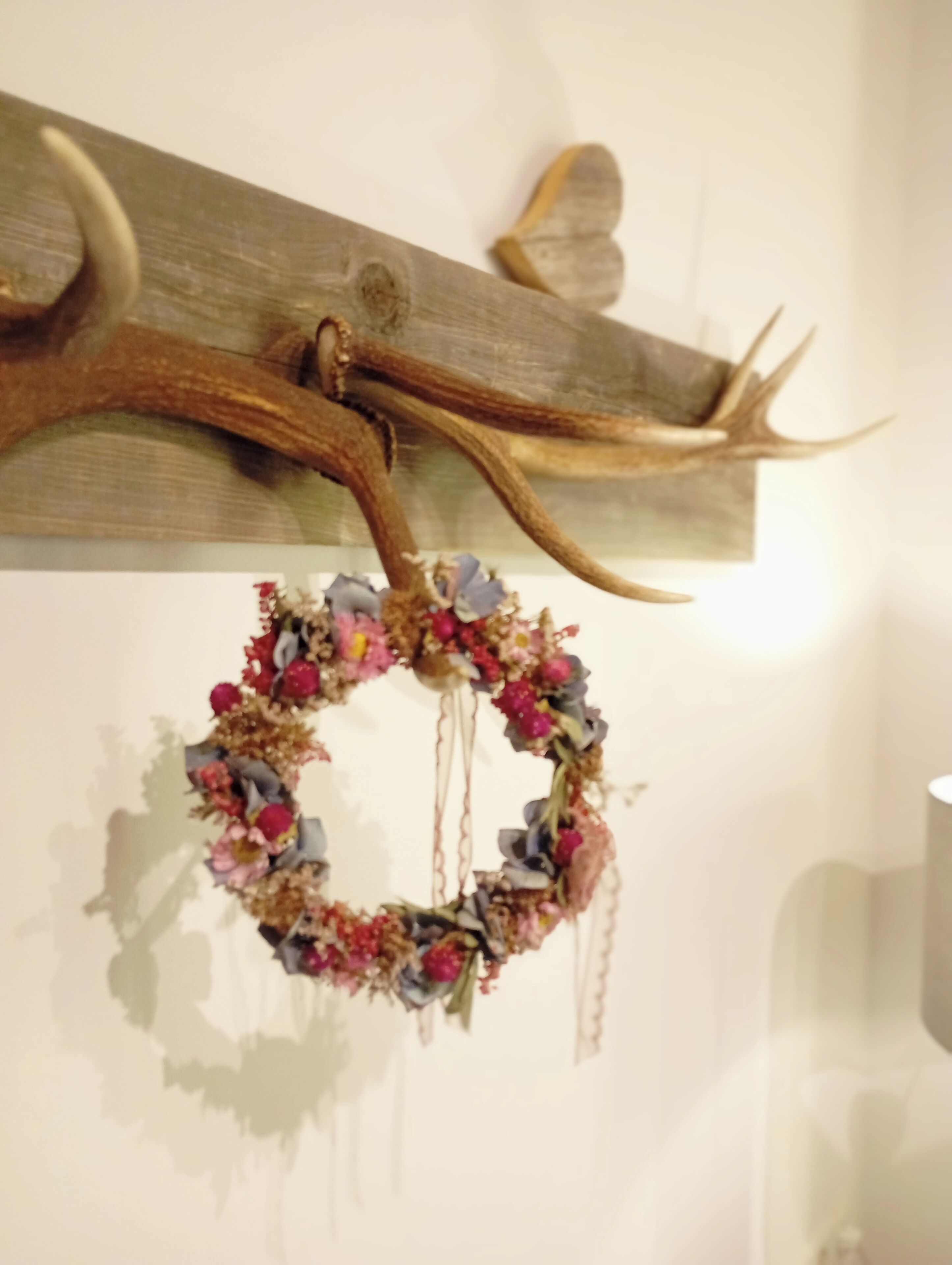 Pared de madera con un cuerno de ciervo montado y una corona de flores.