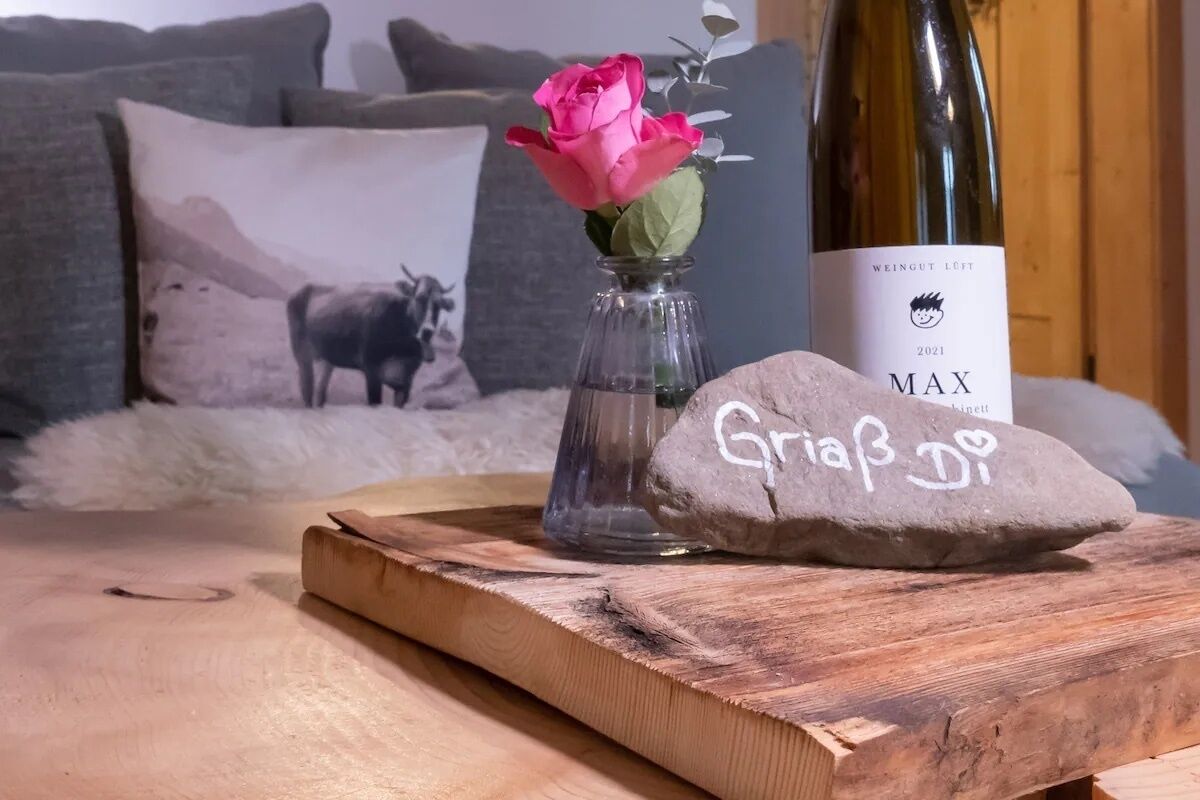 Un tavolo di legno con una bottiglia di vino, un vaso con una rosa rosa e una pietra con del testo.