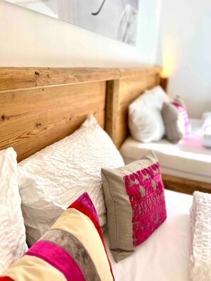 A bed with white and pink pillows, a wooden headboard, and a white wall with a picture frame. - Chalet Alpflower (Halblech)
