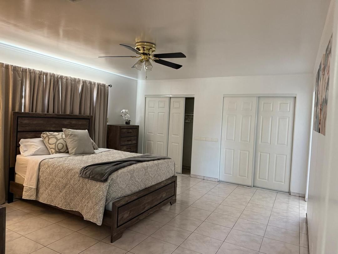 A bedroom with a bed, curtains, a ceiling fan, and a wardrobe.