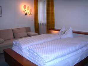 Quarto de hotel com cama de casal, sofá e luminária na parede.
