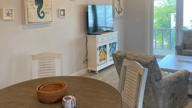 Zona pranzo con un tavolo rotondo, sedie, un televisore su un mobile e opere d'arte alle pareti.