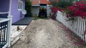 Una strada sterrata conduce a una casa con pareti viola e un pick-up bianco parcheggiato davanti.