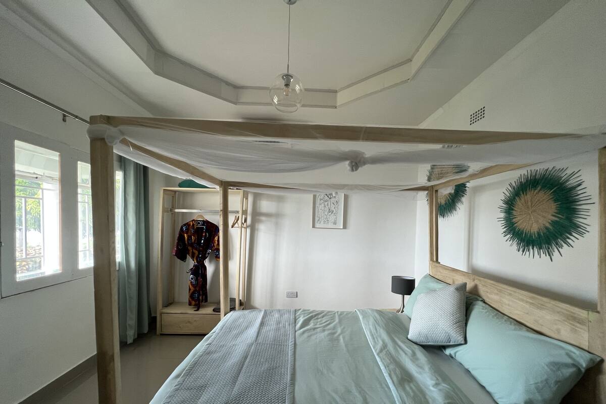 A bedroom with a canopy bed, a bedside lamp, and a decorative wall piece.