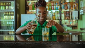 A person pouring a drink into a glass at a bar with shelves of bottles in the background. - Ndau Lodge (Nkhata Bay)