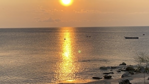 A sunset over a calm sea with boats and rocks. - Ndau Lodge (Nkhata Bay)