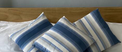 A bed with white bedding and three striped pillows in shades of blue and white.