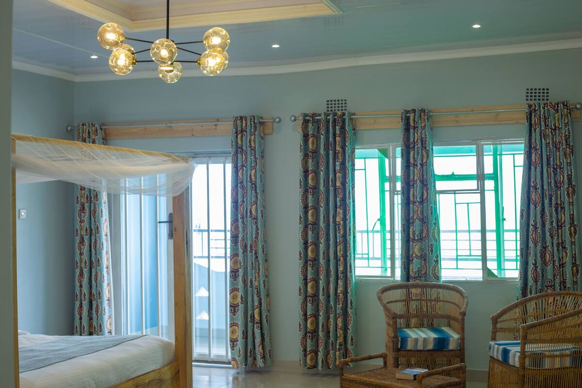 A room with a bed, two wicker chairs, a ceiling light fixture, and patterned curtains.
