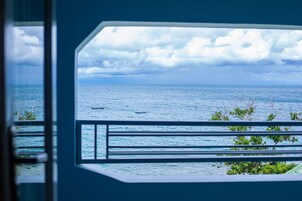A view from a window with a railing, overlooking a body of water and a cloudy sky.