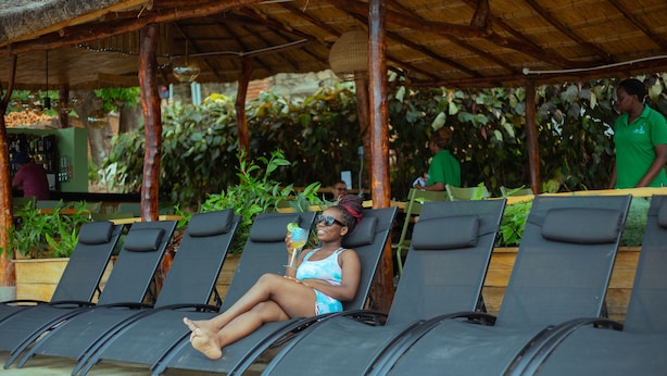 A person lounging on a sunbed under a covered area with a bar in the background. - Ndau Lodge (Nkhata Bay)