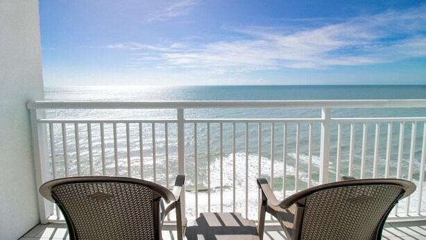 A balcony with two wicker chairs facing a view of the ocean.