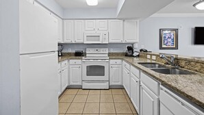 Una cocina moderna con armarios blancos, horno empotrado, microondas, cafetera y pileta doble.