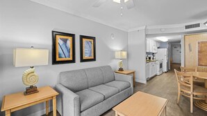 A modern living room with a grey sofa, wooden coffee table, and two lamps. A dining area with a wooden table and chairs is visible.