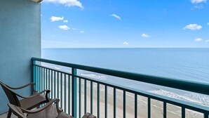 A balcony with a view of the ocean, a chair, and a small table.