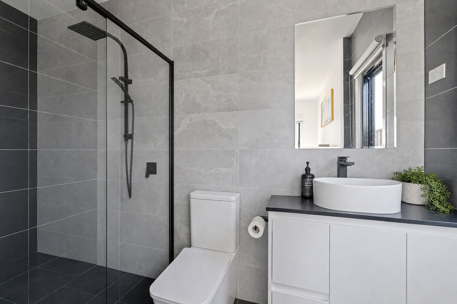 A modern bathroom with a glass-enclosed shower, a white toilet, a sink with a mirror, and a small potted plant.