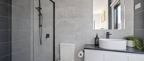 A modern bathroom with a glass-enclosed shower, a white toilet, a sink with a mirror, and a small potted plant.