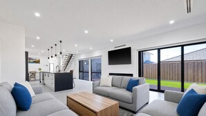 A modern living room with grey sofas, a wooden coffee table, and a kitchen area with a staircase. - Island Family Retreat (Cowes)