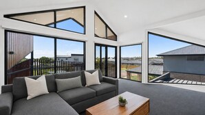 A modern living room with a sectional sofa, a wooden coffee table, and large windows offering a view of the neighborhood. - Island Family Retreat (Cowes)
