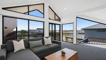 A modern living room with a sectional sofa, a wooden coffee table, and large windows offering a view of the neighborhood.