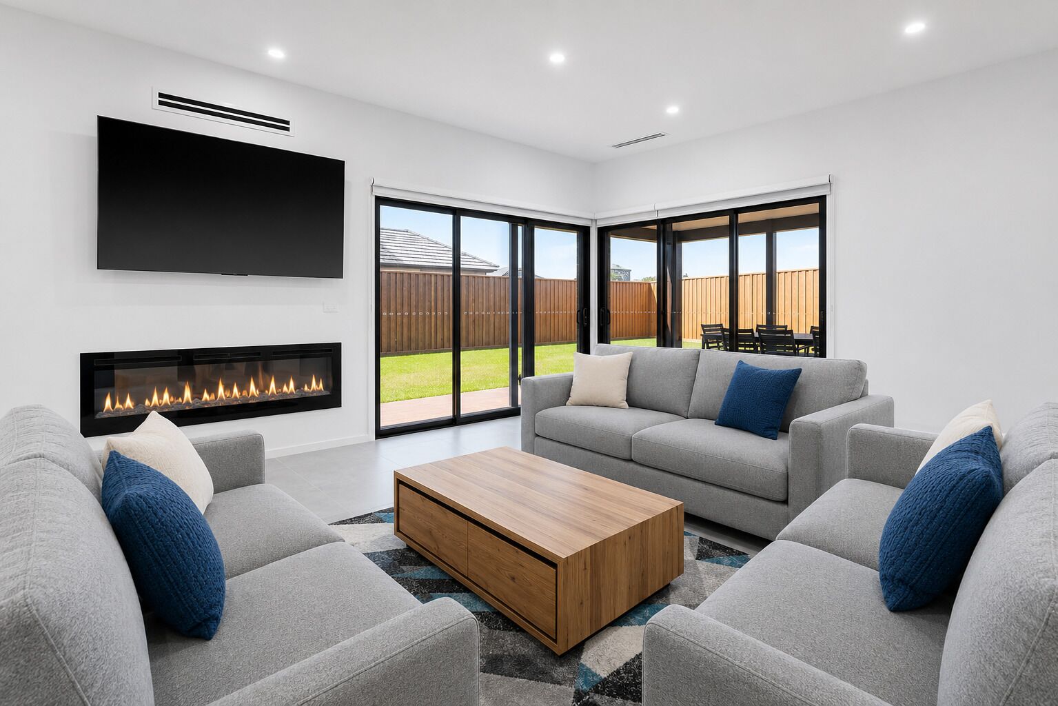 A modern living room with a fireplace, grey sofas, a coffee table, and large windows.