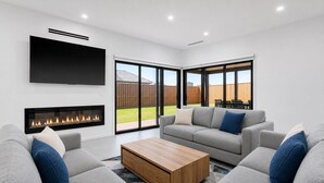 A modern living room with a fireplace, grey sofas, a coffee table, and large windows. - Island Family Retreat (Cowes)