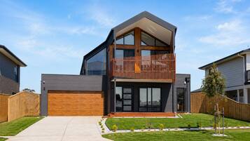A modern two-story house with a large garage, a balcony, and a well-maintained lawn.