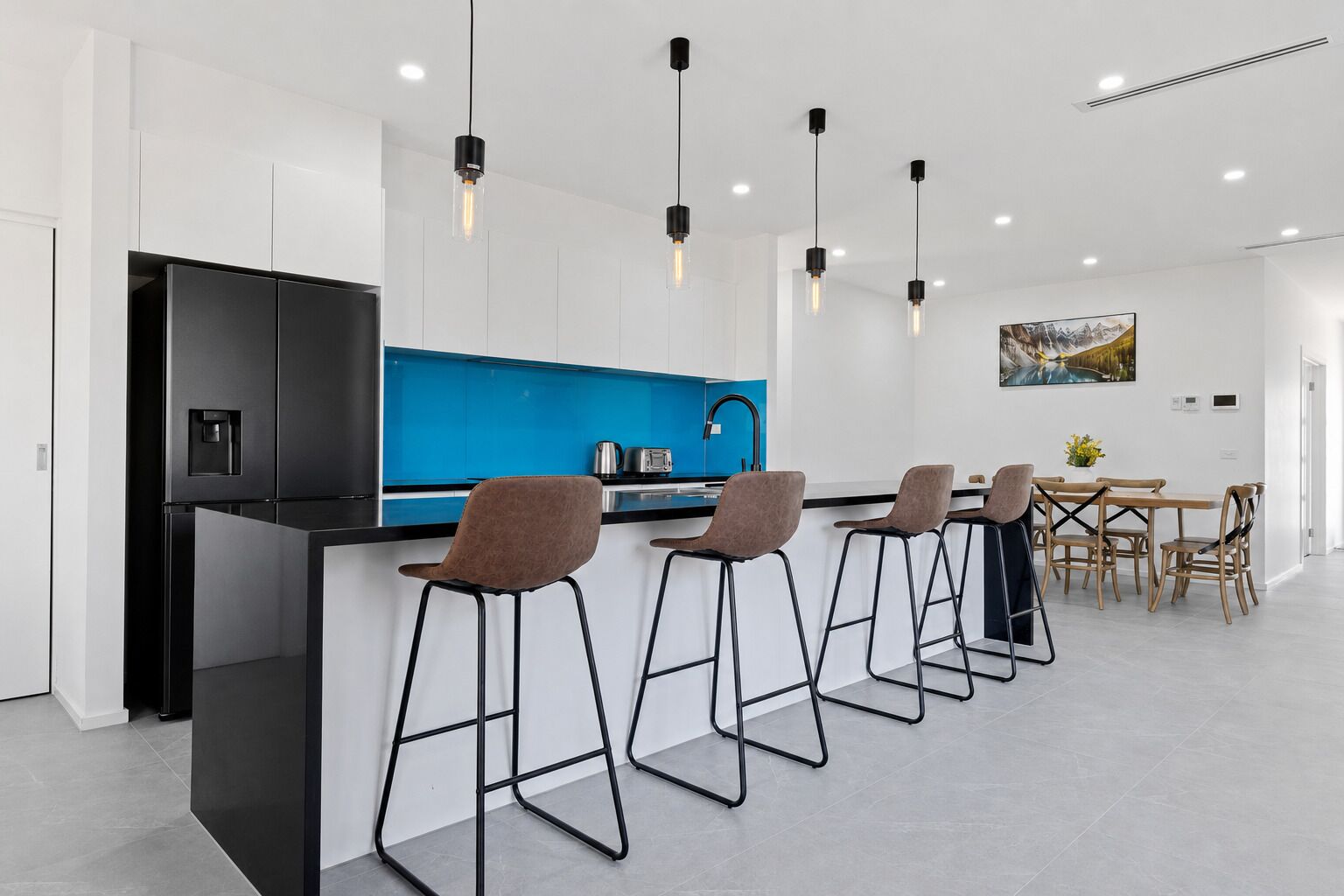 A modern kitchen with a black refrigerator, blue backsplash, and bar stools.