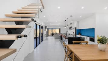 A modern kitchen with a blue accent wall, a dining area with wooden furniture, and a staircase with wooden steps.