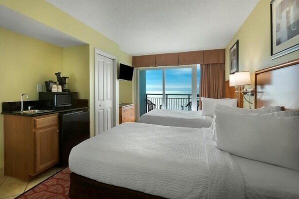 A hotel room with two beds, a kitchenette, a TV, and a balcony with a view.