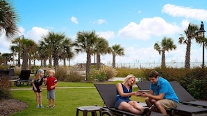 A poolside area with lounge chairs, palm trees, and a view of the ocean.