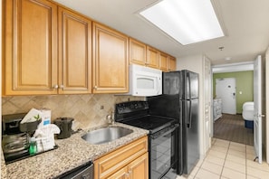 A kitchen with wooden cabinets, a granite countertop, a black stove, a white microwave, and a refrigerator.
