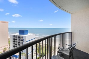 A balcony with a view of the ocean, a chair, and a building with 'INDIO' on it.