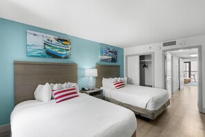 A hotel room with two beds, a wooden headboard, a nightstand with a lamp, and a door leading to a bathroom.