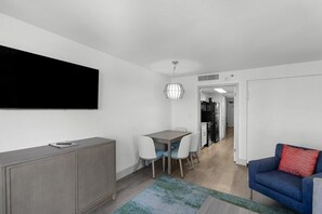 En moderne stue med et fladskærms-tv, et spiseområde med bord og stole, en sofa og et køkken i baggrunden.