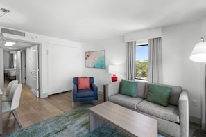 A modern living room with a sofa, armchair, coffee table, and a painting on the wall.