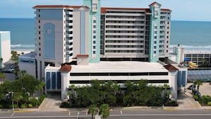 A multi-story hotel with a central atrium, a clock tower, and a view of the ocean. - Coastal Serenity: Ocean View 2 Bdrm Condo 10th Flr (Myrtle Beach)
