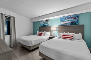 A hotel room with two beds, a window with curtains, and artwork depicting boats on the wall.