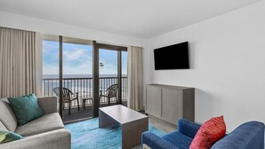 Een moderne hotelkamer met balkon, flatscreen-tv, een bank, een salontafel en uitzicht op zee.
