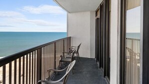 A balcony with two chairs and a table, overlooking a beach and the ocean. - Newly Renovated Ocean View 2 Bdrm Condo 8th Flr (Myrtle Beach)