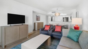 A modern living room with a flat-screen TV, two sofas, a coffee table, and a dining area with a lamp. - Ocean View Retreat 3 Bedroom Condo with a Balcony (Myrtle Beach)