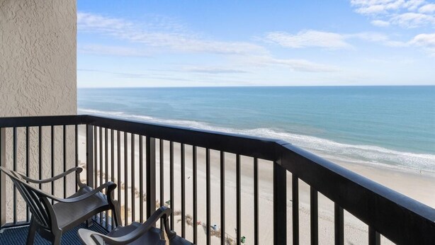 A balcony with a view of the ocean, a chair, and a railing.