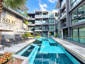 A modern building with a swimming pool, lounge chairs, and a sign that reads 'SILK CONDOMINIUM AO NANG.'